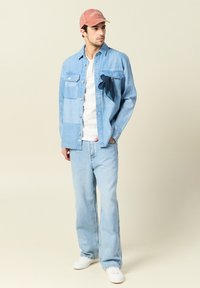 Ljust blå denimjacka med fickor, vit t-shirt, ljusblå jeans och en rosa keps. Accenthalsduk fäst vid jackan. Vita sneakers.