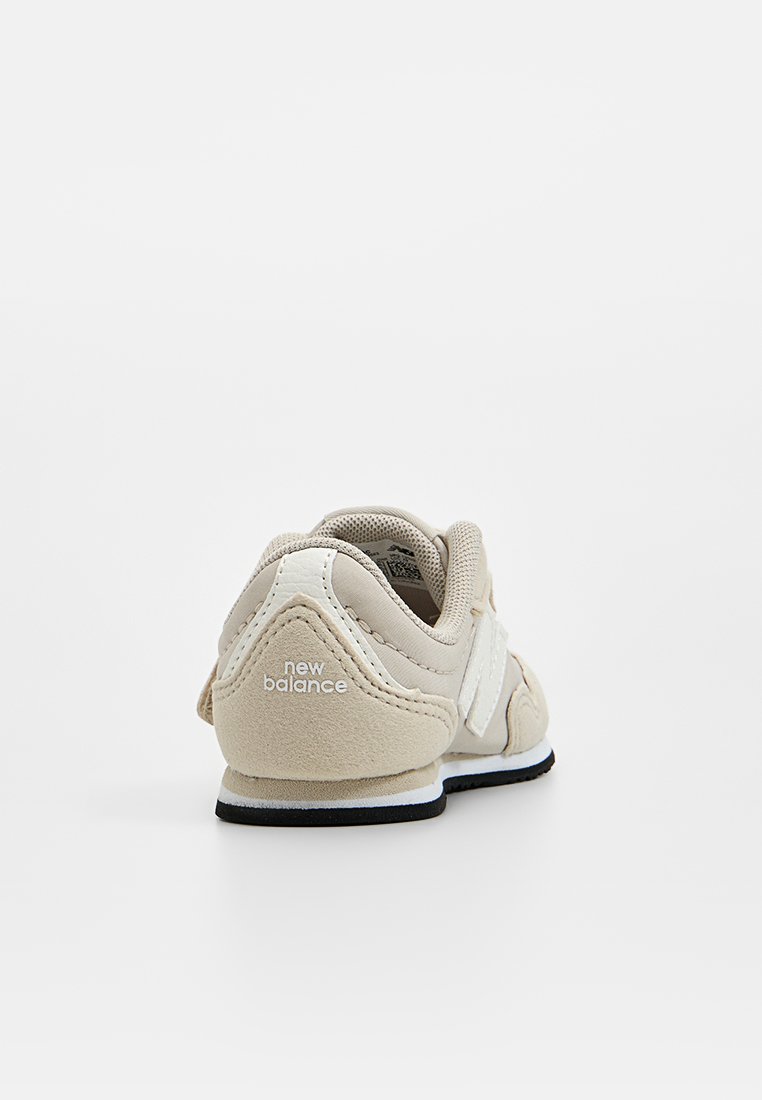 Scarpa sportiva beige con tomaia in suede e mesh, dettagli bianchi, design del tallone curvo e suola nera. Presenta il marchio "new balance" sul tallone.