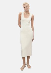 White fitted midi dress with a scoop neckline, made of smooth fabric. Paired with white strappy sandals and a gold bead necklace.