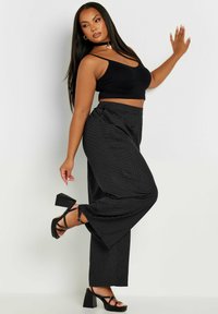 Svart crop top som kombineras med vida svarta byxor med prickar. Modellen bär svarta högklackade sandaler. Slätt tyg, kroppsnära design.