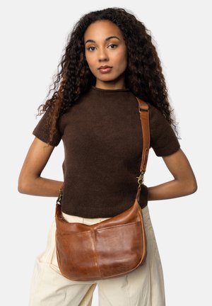 Borsa a spalla in pelle marrone con forma curva, tracolla regolabile e dettagli di cucitura visibili. Sfondo semplice con un modello che la indossa.