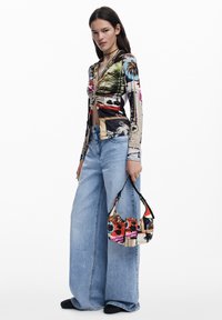 Langärmliges, enganliegendes Oberteil mit einem mehrfarbigen Grafikdruck. Hellblaue, weite Jeans aus Denim, dazu eine kleine Handtasche im Patchwork-Stil.