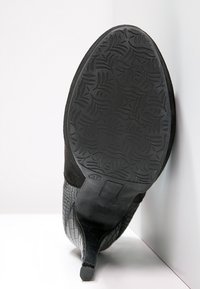 Zapato de tacón alto negro con un patrón de cocodrilo texturizado en la parte delantera y una suela negra lisa que presenta un diseño de relieve floral.