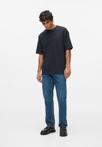 Dunkelblaues, strukturiertes Kurzarm-T-Shirt, kombiniert mit hellblauen Jeans und schwarzen Schuhen, fokussiert auf einen lässigen Schnitt und entspannte Silhouette.