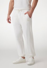 Hvide sweatpants med strammesnor i taljen, sidelommer, teksturerede mesh-paneler og elastiske manchetter, parret med hvide sneakers.