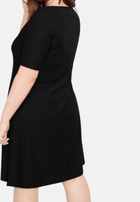 Czarna sukienka z prążkowanego dzianiny, z krótkim rękawem i dopasowanym gorsetem, delikatnie rozszerzająca się na dole. Posiada okrągły dekolt i gładką teksturę.