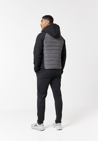 Zwarte en grijze gewatteerde jas met een capuchon, voorzien van een gegarneerde grijze achterkant en gladde zwarte mouwen, gecombineerd met zwarte broek en grijze sneakers.