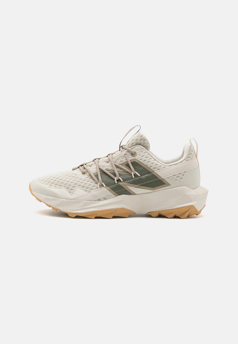 Zapatilla deportiva de color beige claro con detalles laterales verdes, suela intermedia gruesa blanca, suela de goma y cordones beige sobre fondo blanco liso.