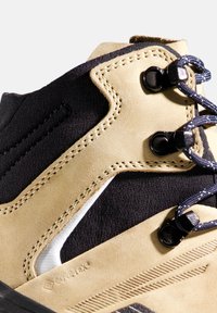 Stivale in tessuto e pelle scamosciata color cammello con dettagli in tessuto nero. Dotato di robusti lacci, occhielli metallici e suola in gomma testurizzata con motivi antiscivolo.