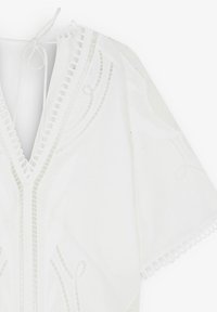 Blouse blanche et légère à manches courtes, ornée de motifs brodés complexes et de finitions à volants le long de l'encolure et des manches.