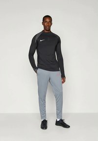 Grå langermet treningstopp med svarte detaljer, kombinert med lysegrå joggebukser med rød logo, og svarte treningssko.