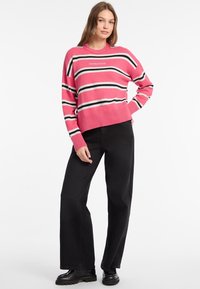 Rosa gestrickter Pullover mit horizontalen schwarzen und weißen Streifen, Rundhalsausschnitt und elastischen Bündchen; kombiniert mit hoch taillierten schwarzen Jeans und schwarzen Stiefeln.