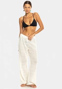 Svart trekantig bikinitopp i kombination med vita, löst sittande texturerade byxor med zickzackmönster och dragsko i midjan.
