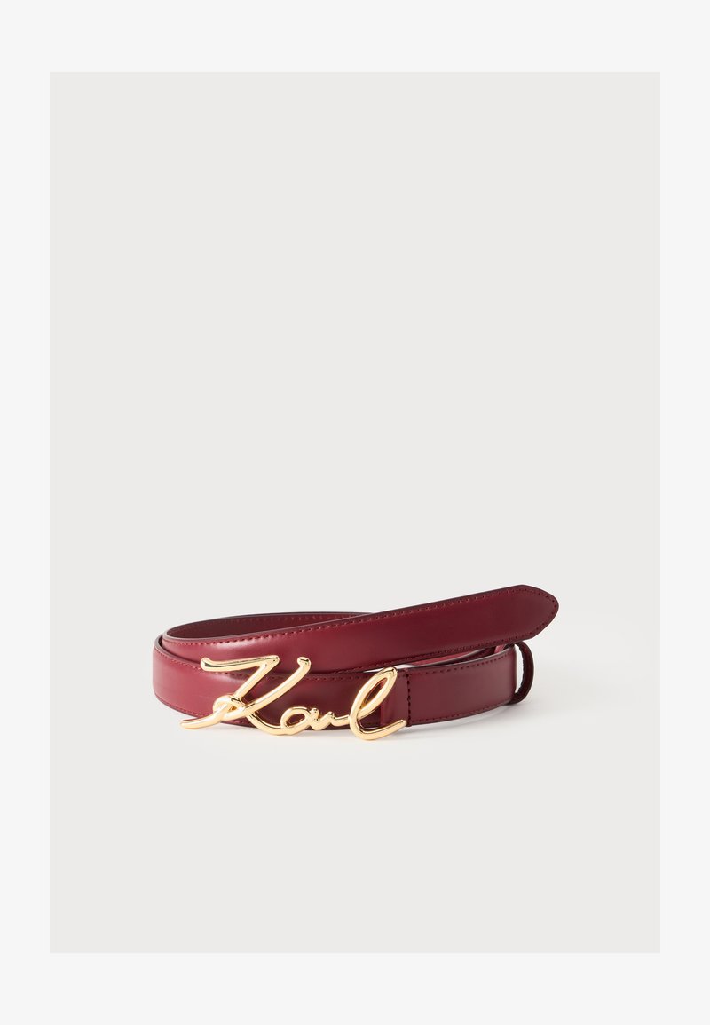 Ceinture en cuir bordeaux avec une boucle dorée en forme du mot "Karl" en écriture cursive, présentée sur un fond blanc.