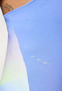 Top deportivo de color azul claro con textura suave, diseño en degradado y sutiles acentos reflectantes a lo largo de la costura lateral.