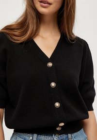 Cárdigan negro de punto con escote en V, mangas cortas y botones redondos decorativos en tono dorado a lo largo del frente. Tejido texturizado.