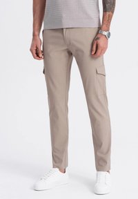 Beżowe spodnie cargo o slim fit, z bocznymi kieszeniami, wykonane z bawełny, o gładkiej teksturze, zestawione z białymi sneakersami.