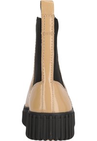 Bottines en cuir verni beige avec des panneaux latéraux élastiques noirs et une semelle en caoutchouc noire, présentant des coutures verticales et un fond texturé.