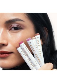Quatre produits à lèvres en tubes crémeux, présentant des bases blanches avec des accents dorés et des noms. Les nuances incluent un rose éclatant, un nude, et d'autres.