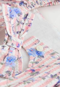 Mehka tkanina z rožnatimi in belimi črtami ter modro-rožnatim cvetličnim vzorcem, na oblačilu z gumbom in nabranim detajlom v obliki pentlje.