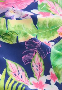 Tissu floral présentant des feuilles roses et vertes vibrantes avec des fleurs blanches sur un fond bleu marine ; texture lisse et design coloré.