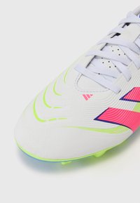 Witte voetbalschoenen met neon groene accenten en roze details. Beschikt over een gestructureerde bovenkant en een patroonontwerp. Inclusief veters.