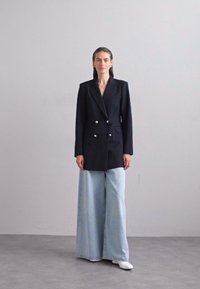 Marineblå dobbeltspent blazer med sølvknapper, kombinert med vide lyseblå jeans. Glatt stoff, strukturert design og fremtredende krager.