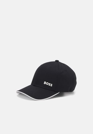 Casquette de baseball noire avec le texte blanc "BOSS" à l'avant et une bordure blanche le long du bord de la visière incurvée, sur fond blanc uni.