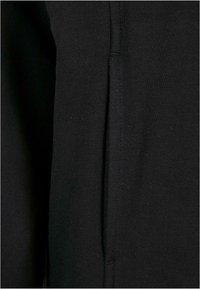 Svart tyg med en slät textur. Har en sömdetalj som löper vertikalt längs kanten, vilket indikerar en design för en pullover eller topp.