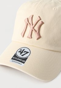 Ρυθμιζόμενο καπέλο του μπέιζμπολ σε κρεμ απόχρωση με ανάγλυφο ροζ κεντητό λογότυπο "NY" και κυκλικό μαύρο και λευκό ταμπελάκι με λεπτομέρειες της μάρκας.