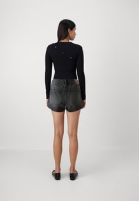Top negro de manga larga con detalle de botones en diagonal, combinado con shorts de mezclilla negros de tiro alto. Tela suave y ajuste casual.