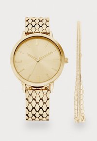 Gold-tone watch with a textured, honeycomb-pattern bracelet, minimalist face with gold hour markers, and two slender chains.