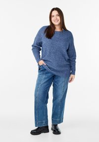 Zils tekstūru adīts džemperis ar brīvu piegriezumu, savienots ar brīvi pieguļošām zilām džinsu biksēm un melniem masīviem zābakiem.