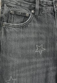 Szürke farmernadrág klasszikus fazonnal, elülső zsebekkel és díszes csillagmintákkal, melyek rhinestone kövekkel vannak díszítve.