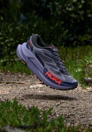 HOKA hardloopschoen met grijze mesh bovenkant, zwarte accenten en rood logo; oversized middenzool en getextureerde rubberen buitenzool voor grip.