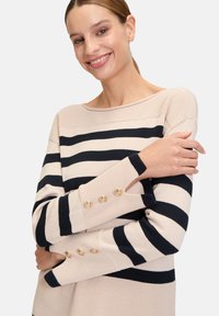 Marineblauw en crèmekleurig gestreepte trui met een bootcut halslijn, textured breiwerk en gouden knopenaccenten op de manchetten. Zacht materiaal, losse pasvorm.