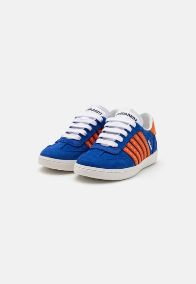 Zapatillas de ante azul con acentos naranjas, cordones blancos y una suela de goma texturizada. Presenta tres rayas naranjas en los lados.
