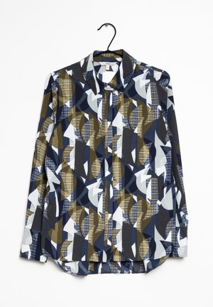 Chemise à manches longues avec col et boutons, présentant un motif géométrique abstrait en bleu marine, olive, gris et blanc, suspendue sur un cintre noir.