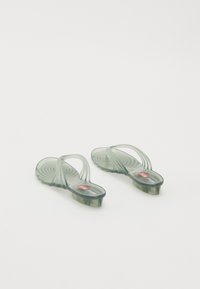 Gennomsiktige grønne plast flip-flops med en teksturert, bølgete design på sålen og en hevet hæl. Logo synlig på fotsengen.