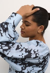Hellblaue Bluse mit schwarzem abstraktem Muster, gepufften langen Ärmeln und strukturiertem Stoff. Verfügt über geraffte Ärmelbündchen für zusätzlichen Detail.
