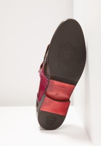 Semelle d’une chaussure habillée en cuir brun et rouge poli présentant des armoiries en relief et des clous métalliques près du talon.