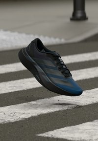 Blue and black athletic shoe hovering above a pedestrian crosswalk on a city street.