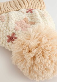 Strikket off-white hue hat med en ribbet beige kant, med pink blomsterbroderi og en stor beige pom-pom på toppen.