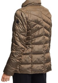 Veste matelassée marron avec couture en chevron portée par une personne vue de dos et de côté, avec un pantalon noir visible.