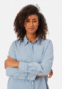 Camicia in denim blu chiaro con chiusura a bottoni, maniche lunghe e colletto classico. Tessuto morbido e dettagli cuciti sui polsini.