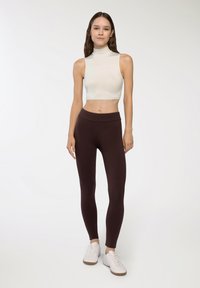 Dopasowany kremowy crop top z wysokim kołnierzem w połączeniu z legginsami w ciemnym brązie o wysokim stanie. Całość uzupełniają białe trampki. Prosty, elegancki design.