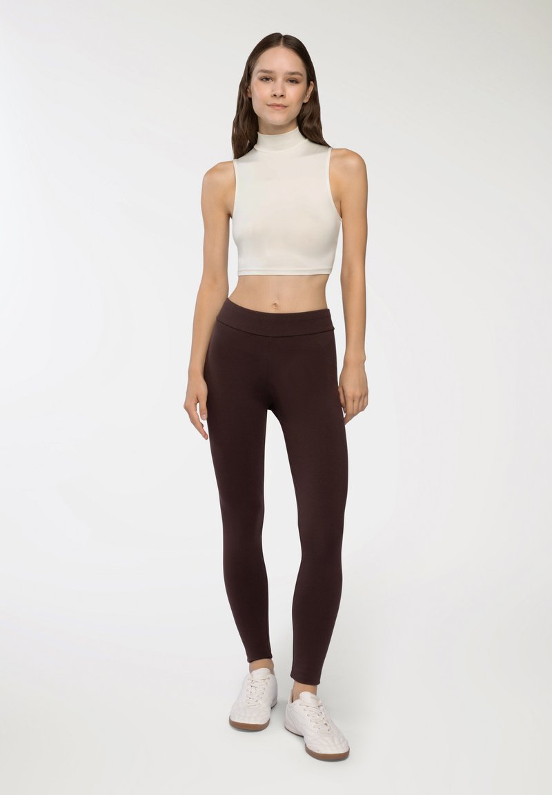 Dopasowany kremowy crop top z wysokim kołnierzem w połączeniu z legginsami w ciemnym brązie o wysokim stanie. Całość uzupełniają białe trampki. Prosty, elegancki design.
