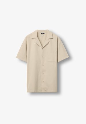 Chemise beige à manches courtes avec boutons, col de style camp et poche poitrine, présentée à plat sur un fond blanc.