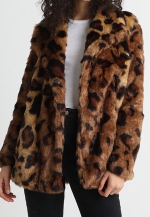 Manteau en fausse fourrure imprimé léopard marron et noir porté sur un haut côtelé blanc et un pantalon noir.