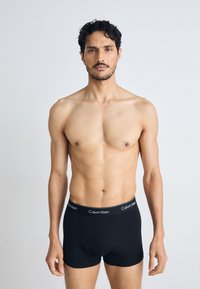 Zwarte katoenen boxershorts met een aansluitend ontwerp, voorzien van een zwarte tailleband met de tekst "Calvin Klein" in witte letters.